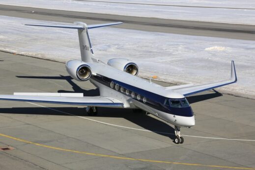Charter-a ltd white and blue private jet parked on an airport apron with snow on the ground behind it.